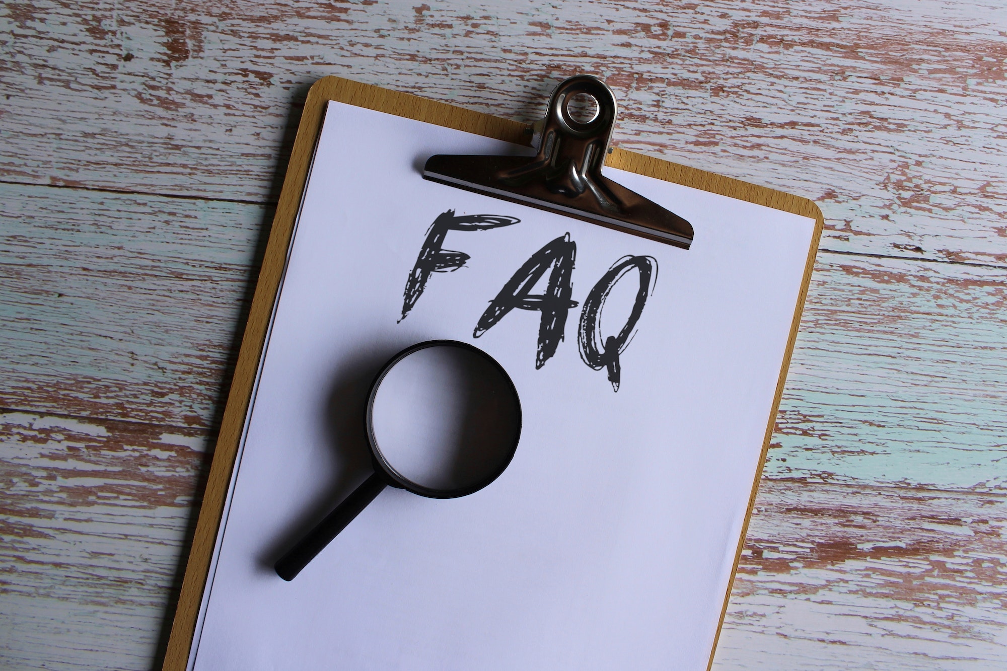 Paper clipboard with text FAQ or frequently asked question and magnifying glass.